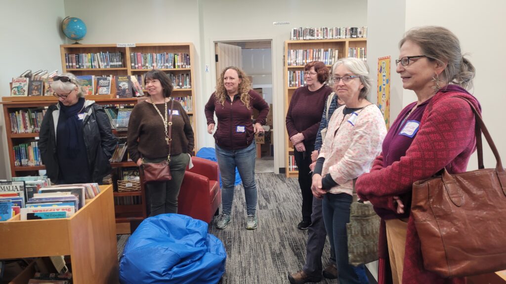 Group of women standing in a library room with bookshelves and books.