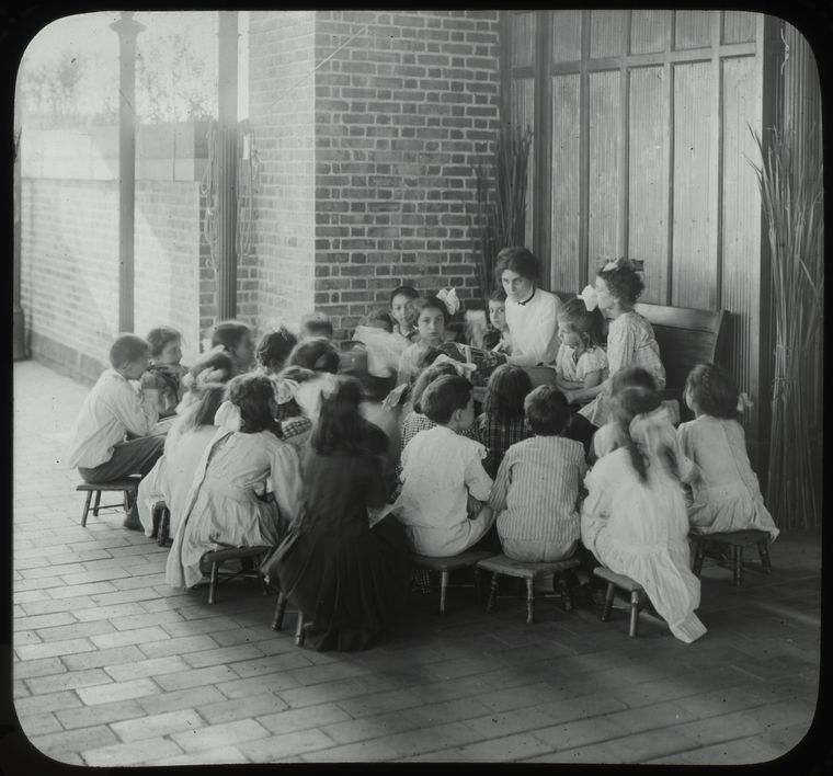 Black and white photograph of a woman reading to a group of children outside